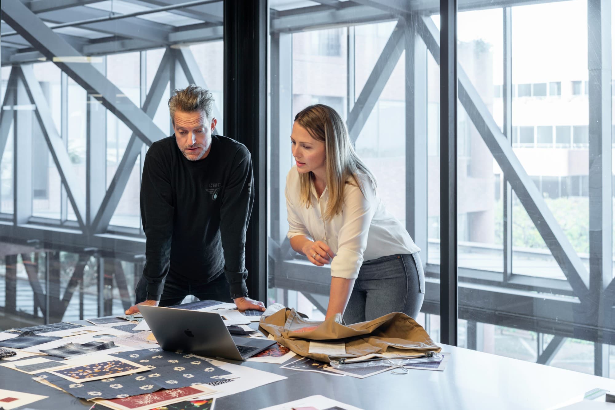 Two designers reviewing fabric samples and a laptop in a bright studio
