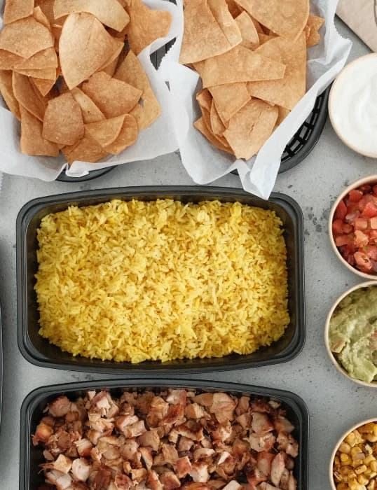 Catering spread of chips, rice, chicken and toppings